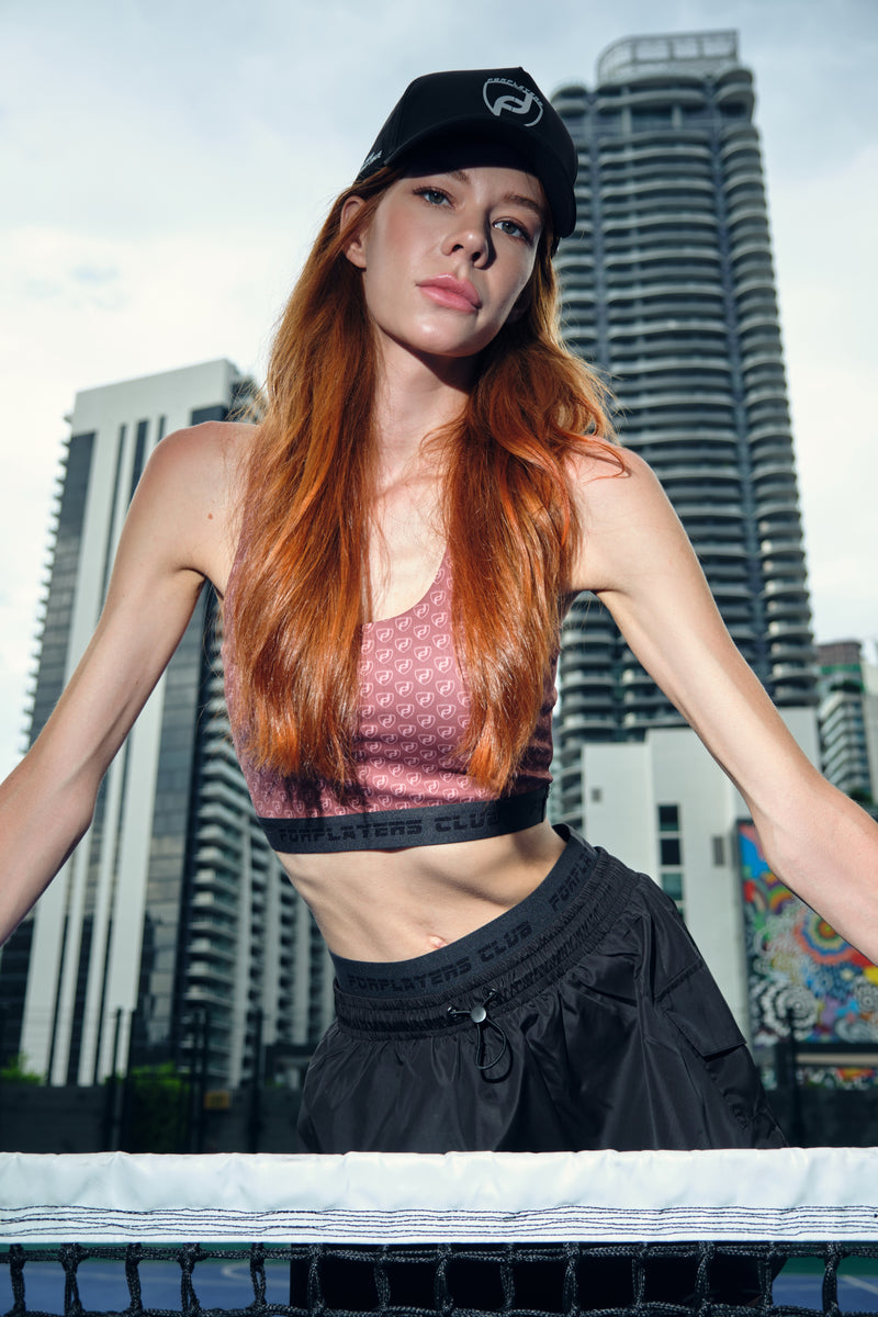Model seated in black tennis skirt and sports bra